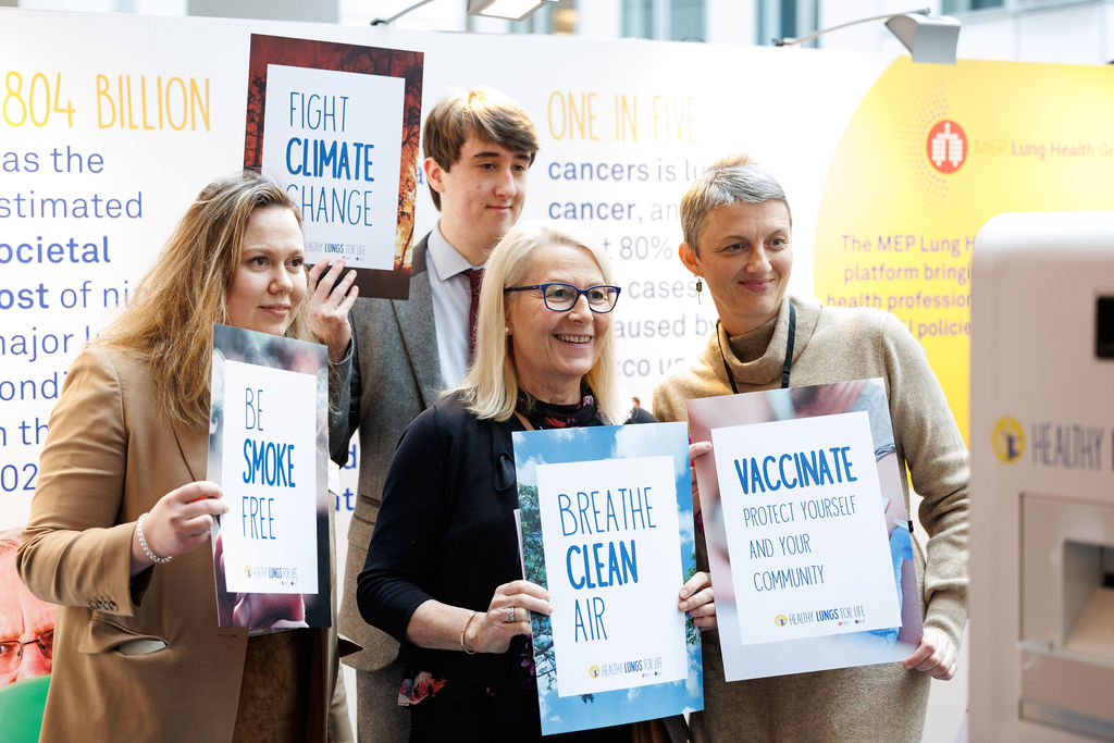 Attendees at the Healthy Lungs for Life exhibition in the European Parliament pose at the photo booth holding signs related to the campaign's themes. The signs read: "breathe clean air", "be smoke free", "vaccinate" and "fight climate change"